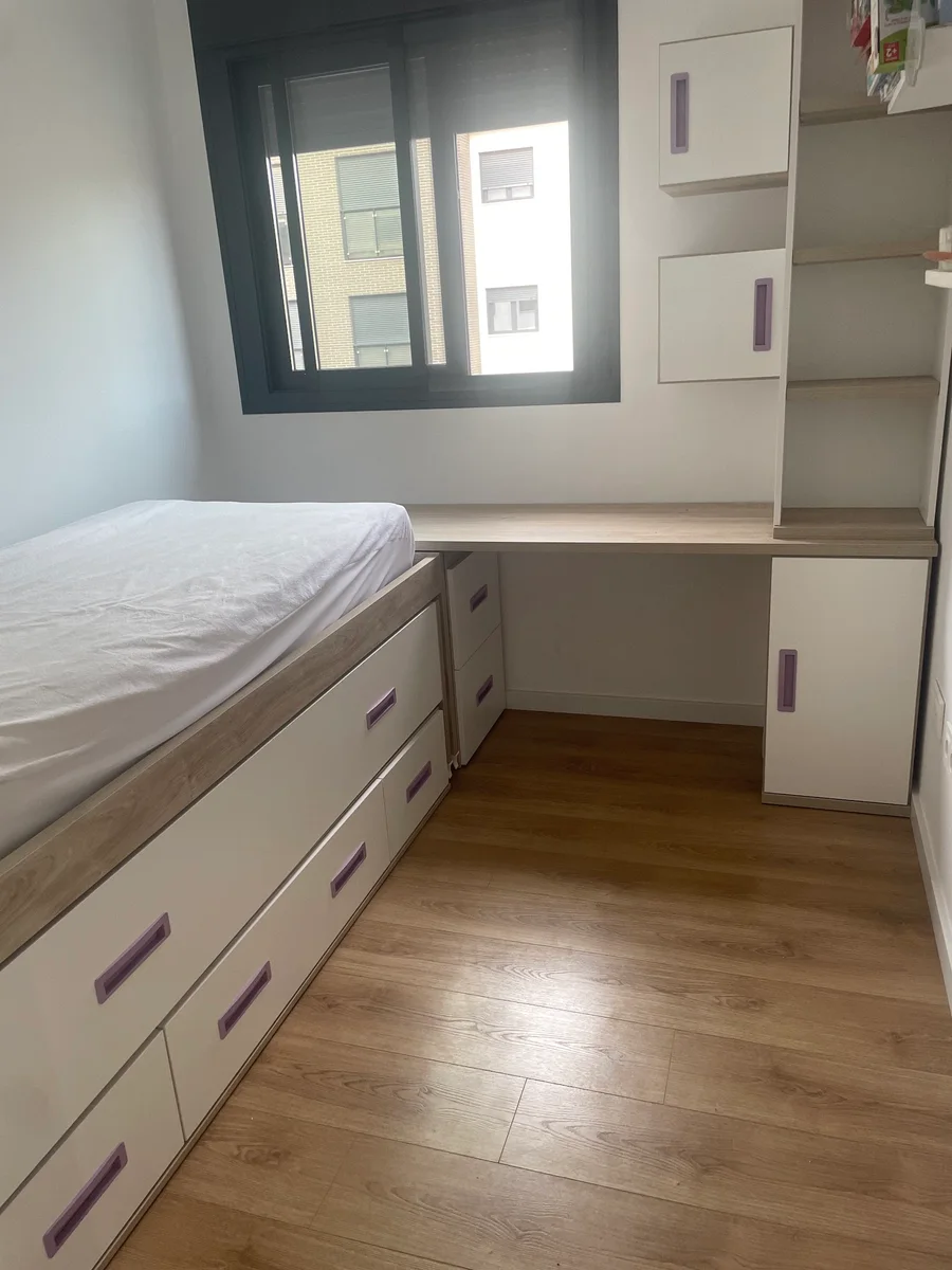 Dormitorio infantil con cama nido de cajones, escritorio corrido bajo la ventana y módulos altos con tiradores lila.